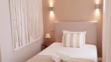 A hotel room with a bed, a nightstand, a lamp, and a wall-mounted light fixture.