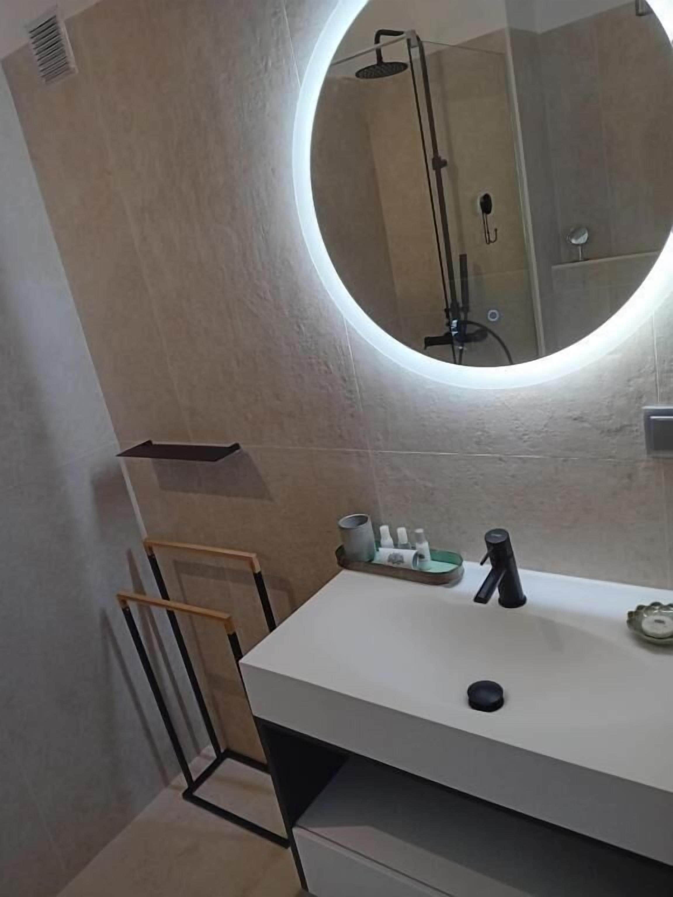 A bathroom with a round mirror, a white sink, and a shower area.