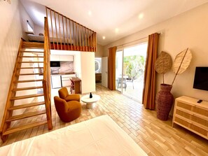 A hotel room with a bed, a sofa, a small table, a TV, a staircase, and a sliding door leading to an outdoor area. - Studio Ti'Kay - Terrace 4 pers, 3mn from Anse Mitan beach (Les Trois-Îlets)