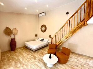 A bedroom with a bed, a small table, two chairs, a wooden staircase, and a wall-mounted air conditioner. - Studio Ti'Kay - Terrace 4 pers, 3mn from Anse Mitan beach (Les Trois-Îlets)