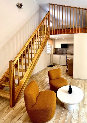 A modern interior with a wooden staircase, two armchairs, a round coffee table, and a kitchen area. - Studio Ti'Kay - Terrace 4 pers, 3mn from Anse Mitan beach (Les Trois-Îlets)