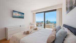 Ein Schlafzimmer mit einem großen Bett, einem Fernseher an der Wand und Blick auf das Meer.