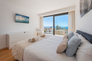 Ein Schlafzimmer mit einem großen Bett, einem Fernseher an der Wand und Blick auf das Meer.