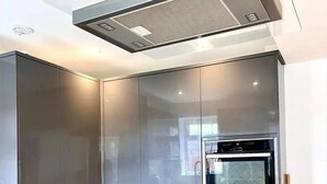 A modern kitchen with a built-in oven, a glass-fronted cabinet, and a sleek black induction cooktop. - Tranquil Turquoise - 3 Bed House With Parking (Bracknell)