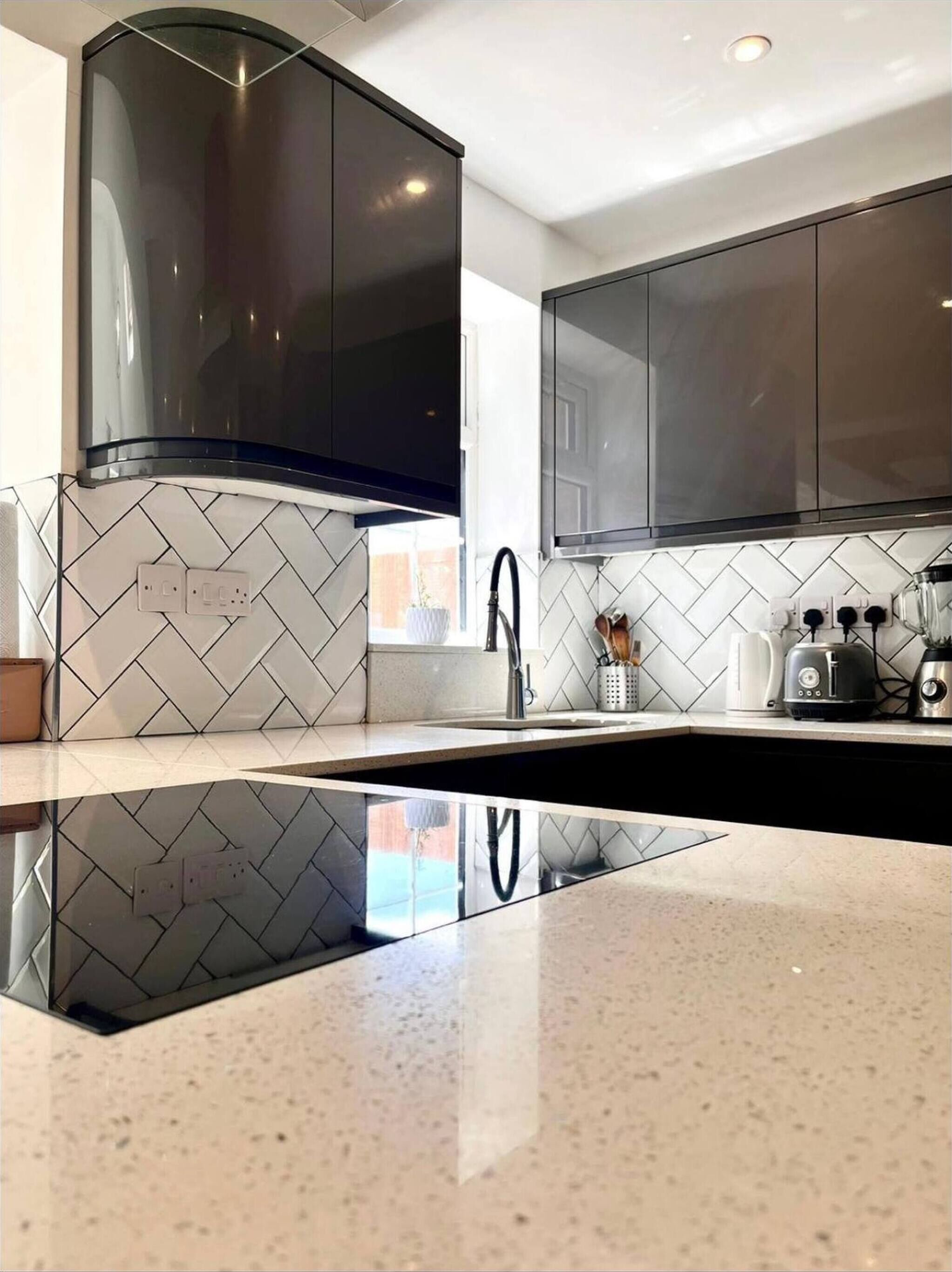A modern kitchen with black cabinets, a stainless steel range hood, and a white tiled backsplash.