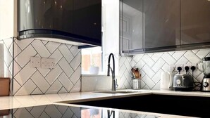 A modern kitchen with black cabinets, a stainless steel range hood, and a white tiled backsplash. - Tranquil Turquoise - 3 Bed House With Parking (Bracknell)