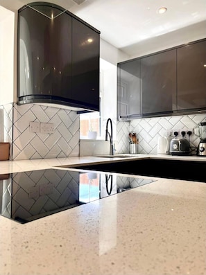 A modern kitchen with black cabinets, a stainless steel range hood, and a white tiled backsplash. - Tranquil Turquoise - 3 Bed House With Parking (Bracknell)