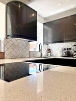 A modern kitchen with black cabinets, a stainless steel range hood, and a white tiled backsplash.