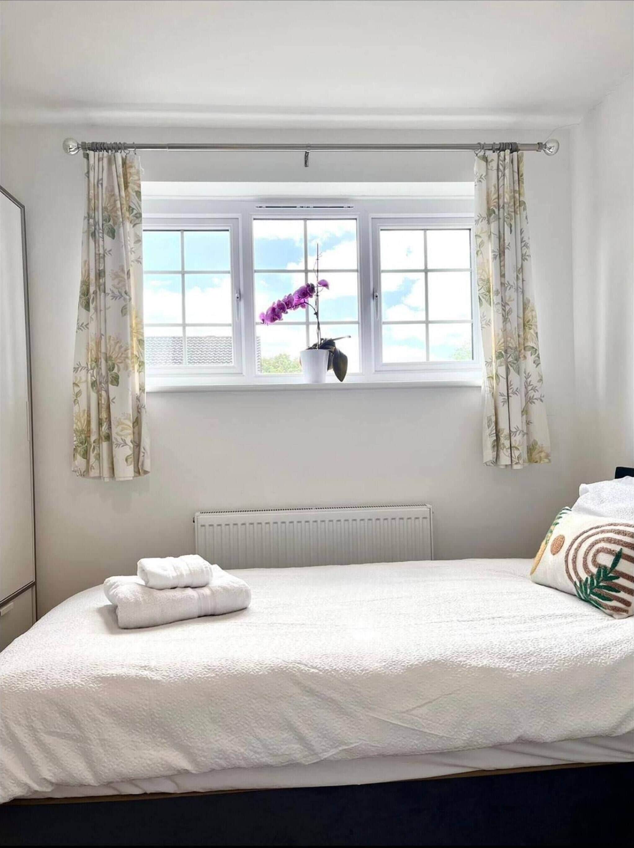 A bedroom with a bed, a window with curtains, a radiator, and a potted plant.