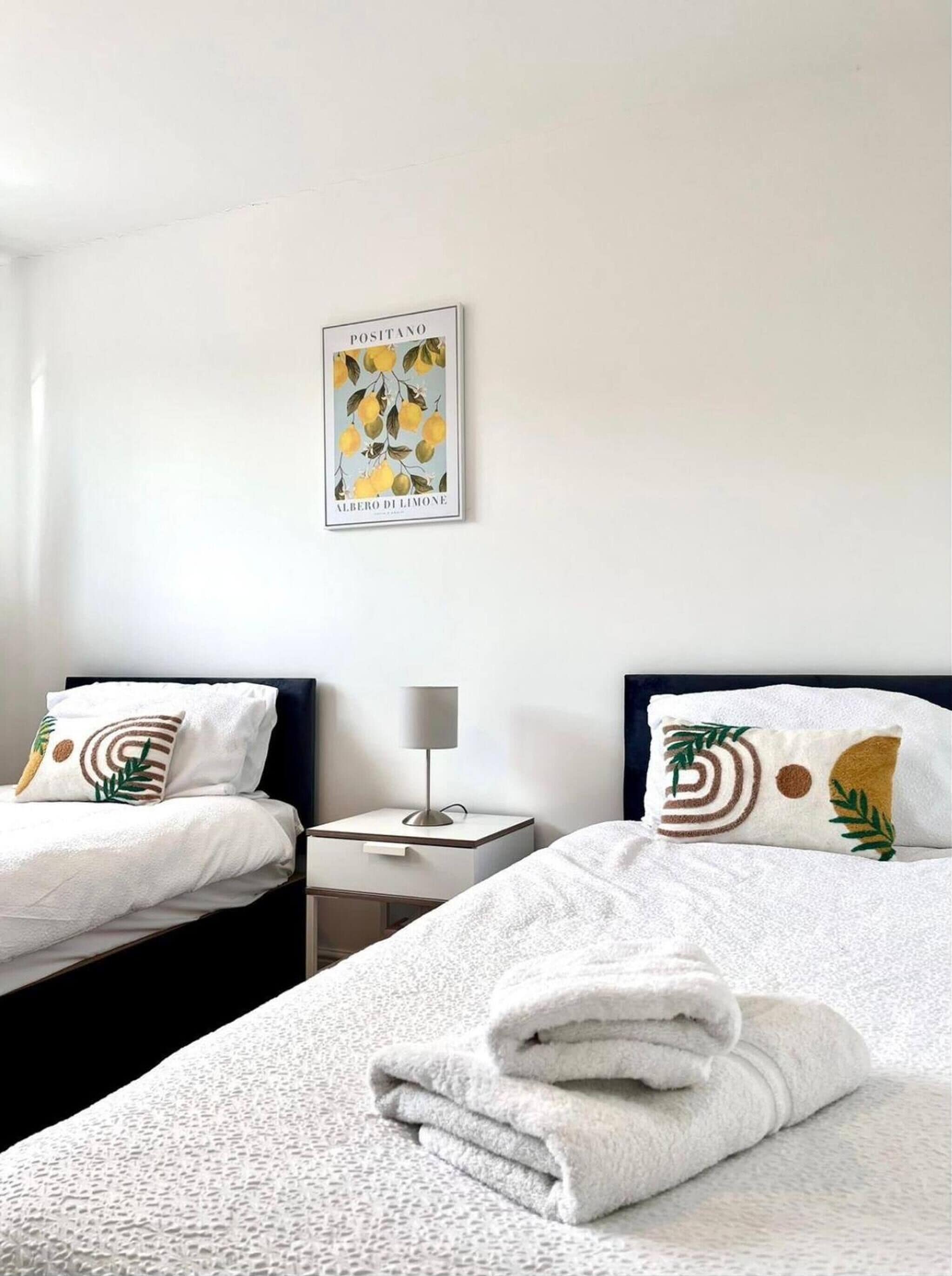 A hotel room with two beds, a nightstand with a lamp, and a wall-mounted picture.