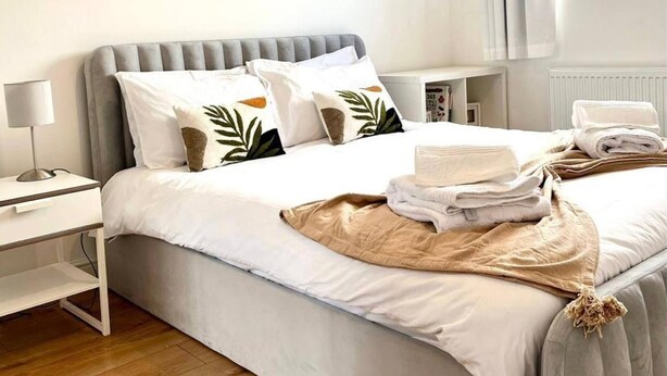 A neatly made bed with white bedding, a grey headboard, and a bedside table with a lamp. - Tranquil Turquoise - 3 Bed House With Parking (Bracknell)