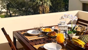 Ein Balkon mit Frühstückstisch, Blick auf eine Küstenstadt.