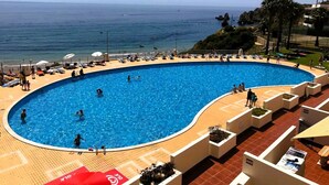 Ein großer Außenpool mit geschwungener Kante, umgeben von Liegestühlen und Blick auf das Meer.