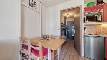 A compact kitchen with a dining table, chairs, a microwave, and a refrigerator.