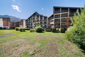 Un hôtel à plusieurs étages, doté de balcons, d’une pelouse bien entretenue et surplombant un paysage montagneux.