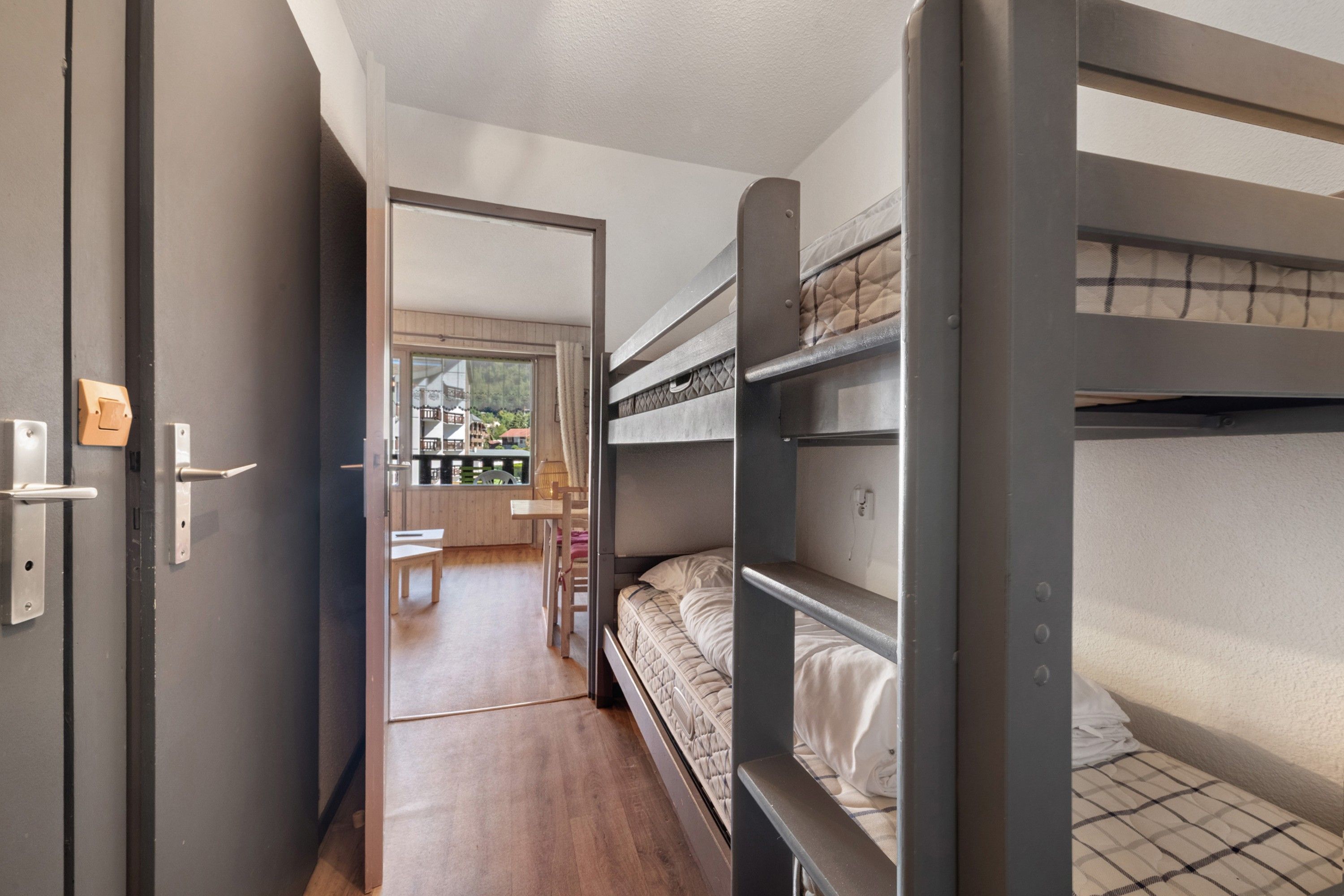 Une chambre compacte avec des lits superposés, un plancher en bois et une vue sur un balcon aménagé avec du mobilier d’extérieur.