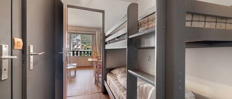 Une chambre compacte avec des lits superposés, un plancher en bois et une vue sur un balcon aménagé avec du mobilier d’extérieur.
