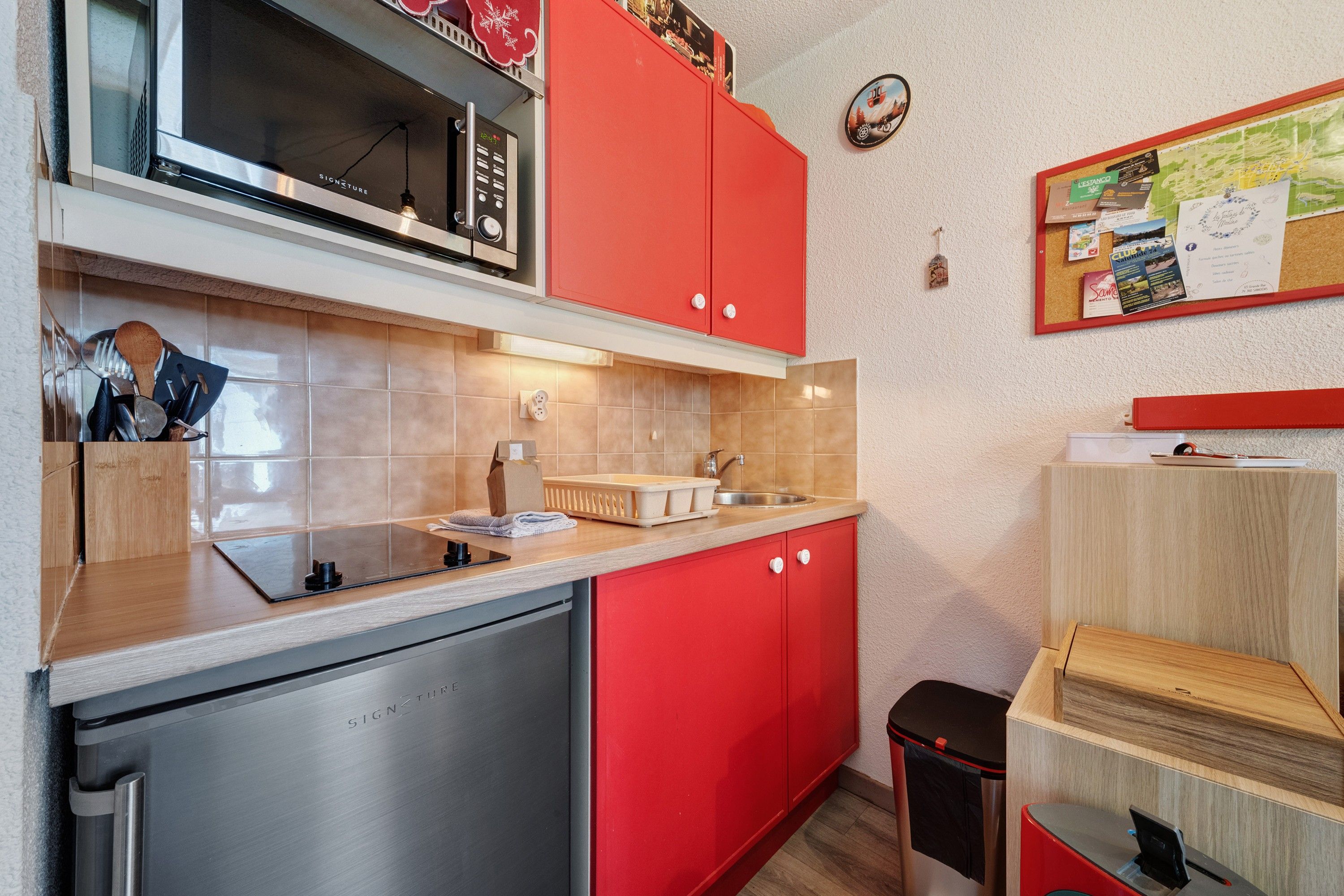 A modern kitchen with stainless steel appliances, red cabinetry, and a wooden countertop.