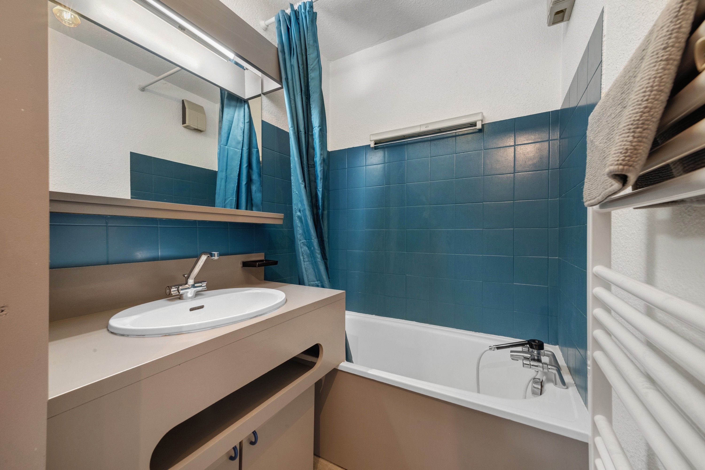 Un baño con un lavamanos blanco, un espejo, un perchero para toallas y una bañera.
