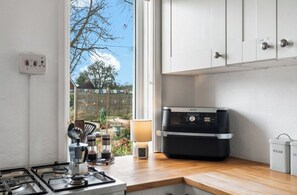 Et køkken med gaskomfur, en Ninja blender og et vindue med udsigt til en baghave.