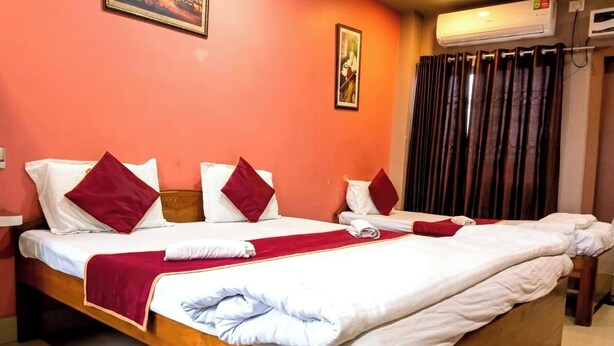 Een hotelkamer met twee bedden, rood-wit beddengoed, een rode plaid en een luchtverkoeler bevestigd aan de muur.