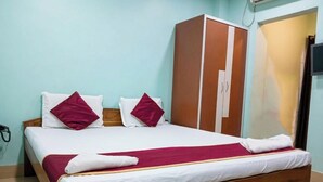 Een keurig opgemaakt bed met witte en bordeauxrode beddengoed, een houten hoofdbord en een garderobe met spiegel.
