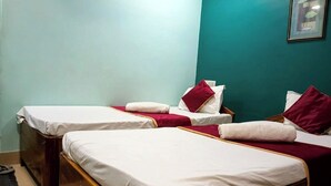 Een kamer met twee bedden, elk voorzien van witte lakens en rode kussens, tegen een achtergrond van teal muren.