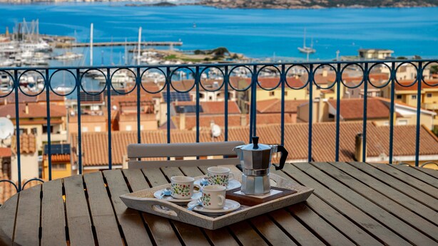 A balcony with a table set for two, overlooking a marina and coastal town. - Holiday Home 'Mariella' with Sea View and Private Terrace (Palau)
