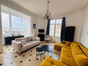 A living room with a beige sofa, a yellow sofa, a small round table, a white armchair, and a TV on the wall. - Exceptional seaside stay with breathtaking views (3* villa) (Villers-sur-Mer)