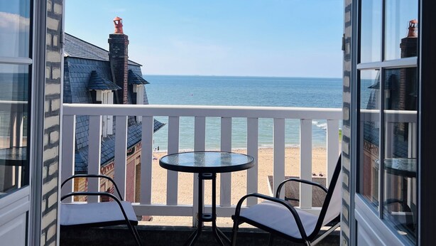 Ein Balkon mit Blick auf den Strand, zwei Stühle und ein kleiner Tisch.
