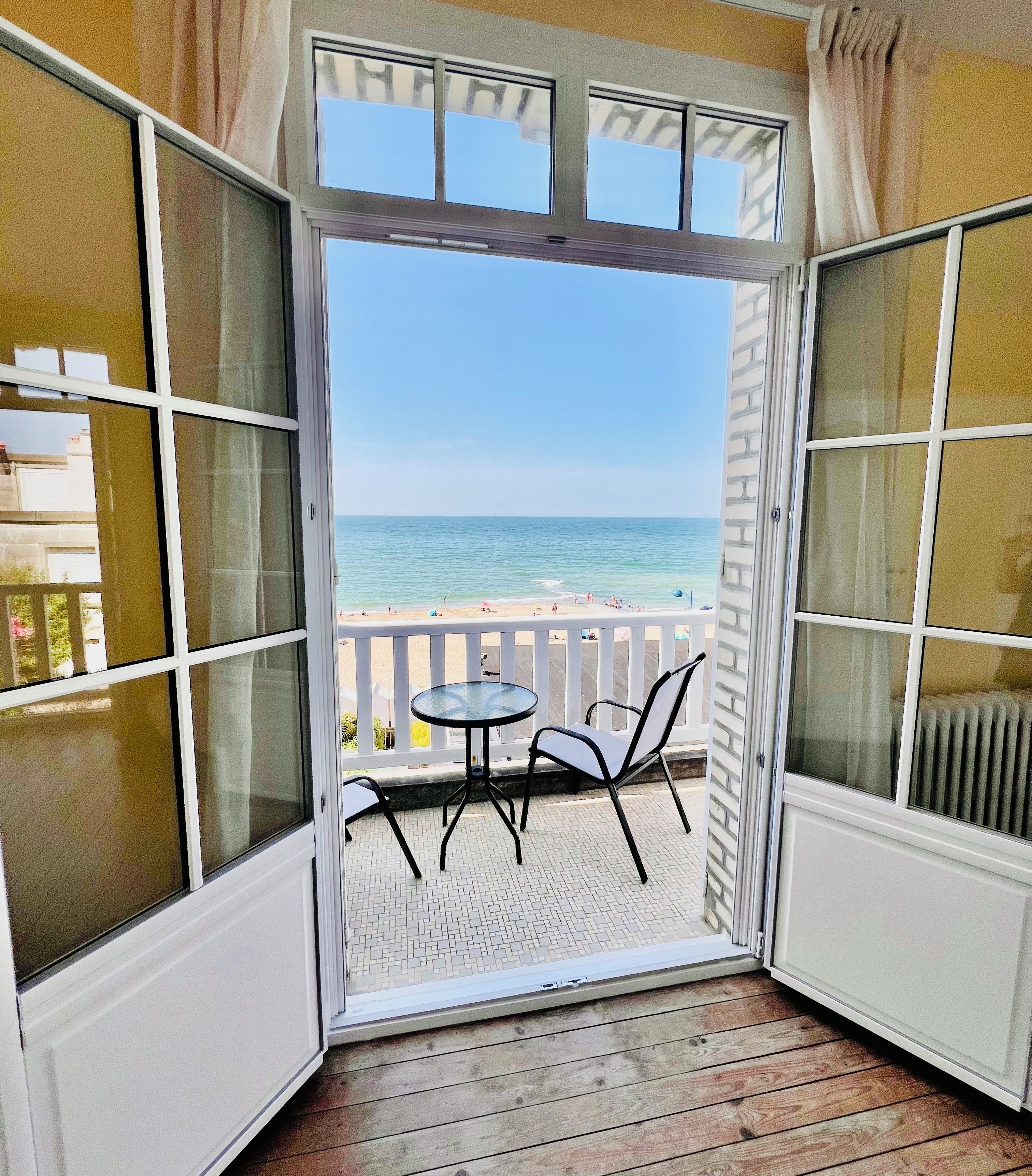 A balcony with a view of the beach and ocean, featuring a table and chairs.