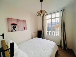 A bedroom with a large bed, a radiator, a window with curtains, and a wall-mounted artwork.
