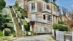 Ein großes, historisches Gebäude mit einer steilen Treppe zum Eingang, umgeben von gepflegten Hecken.