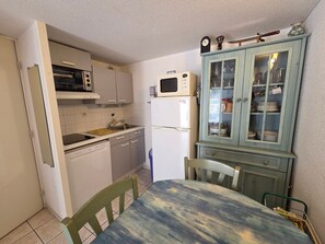 A compact kitchen with a microwave, oven, and refrigerator. There is a dining table with chairs and a cabinet with glass doors. - Charming cottage - 5 guests (La Tranche-sur-Mer)