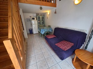 A cozy room with a purple sofa, a wooden table, a green cabinet, and a tiled floor. - Charming cottage - 5 guests (La Tranche-sur-Mer)