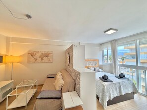 A modern hotel room with a sofa, a small desk, a map on the wall, and a view of the city through large windows. - Terrasol EL Cisne Torre DEL MAR (Velez-Malaga)