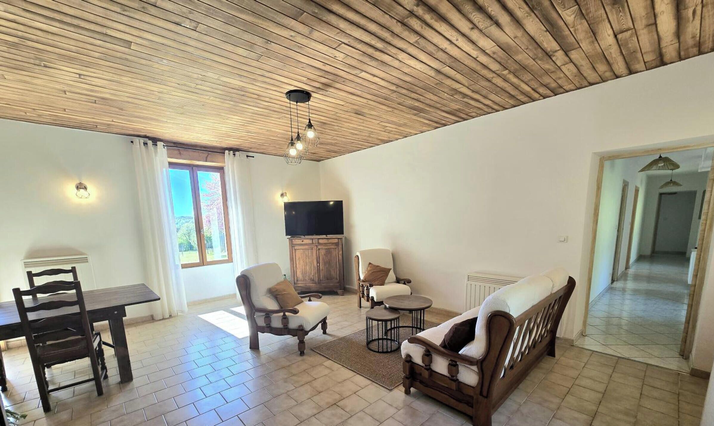 Un salon avec un plafond en bois, un téléviseur, une table à manger avec des chaises et un canapé.