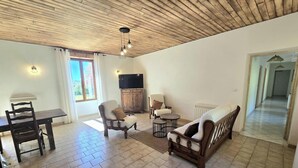 Ein Wohnzimmer mit Holzboden, einem Fernseher, einem Esstisch mit Stühlen und einem Sofa.