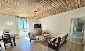 Una sala de estar con techo de madera, un televisor, una mesa de comedor con sillas y un sofá.