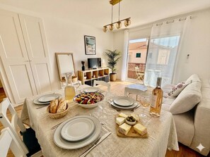 A dining area with a table set for four, including plates, glasses, and a bottle of wine. - Air-conditioned apartment, balcony - 4 guests (Le Lavandou)