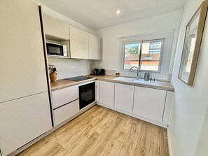 A compact kitchen with white cabinets, a microwave, a stove, and a sink. - Air-conditioned apartment, balcony - 4 guests (Le Lavandou)