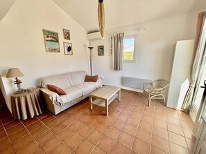 Ein Wohnzimmer mit einer Couch, einem kleinen Tisch, einer Lampe, einem Sessel und einem Fenster mit Vorhängen.