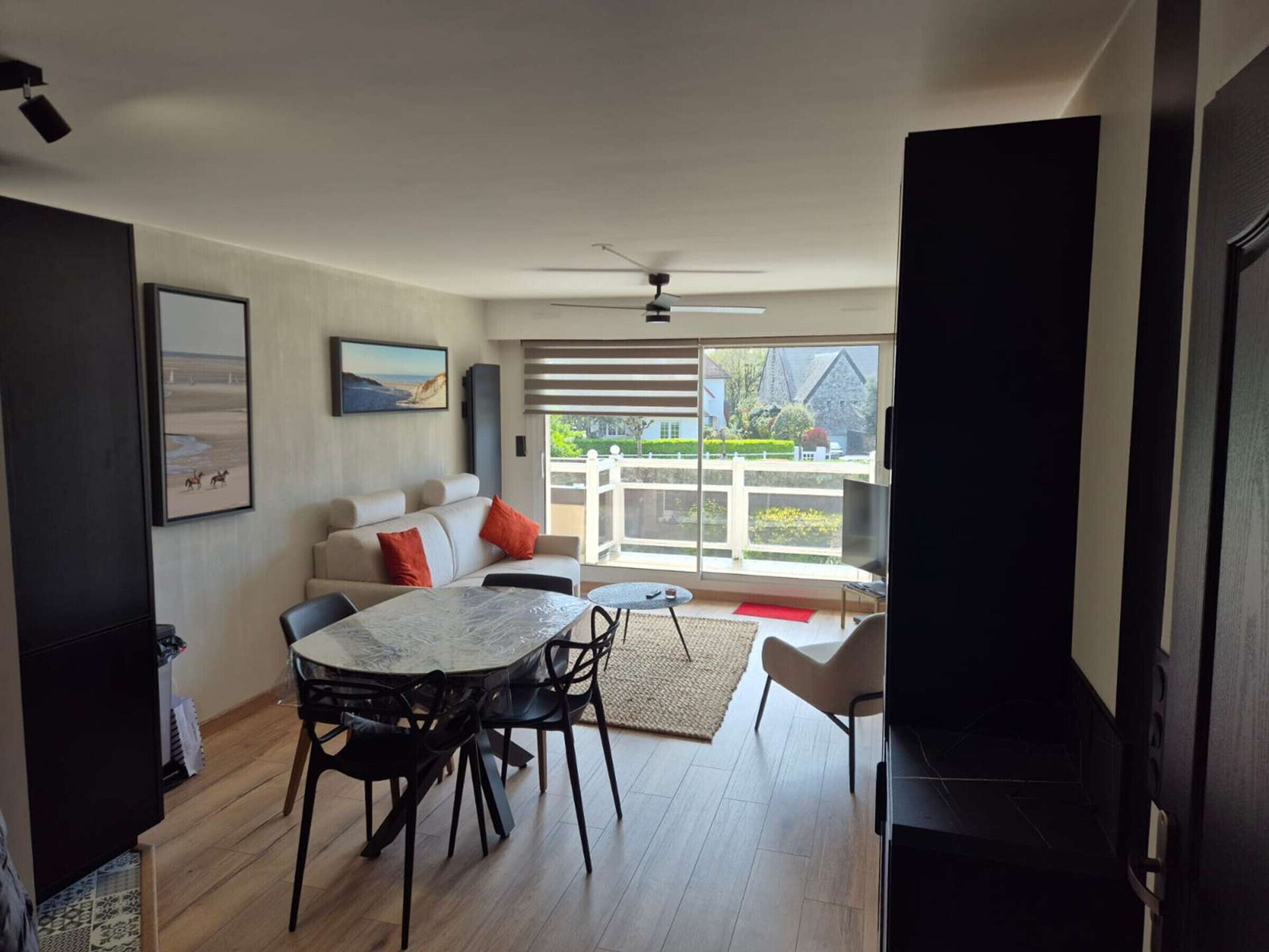 A modern living room with a sofa, dining table, and chairs, a television, and a balcony with a view.