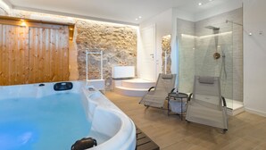 A spa area with a hot tub, two lounge chairs, a small table, and a stone wall. - Villa Raggio di Luce Stigliano (Sovicille)