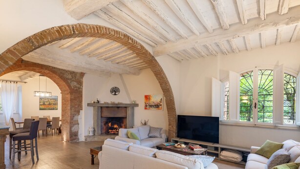 A spacious living area with a fireplace, sofas, a television, and a dining area with chairs and a table. - Villa Raggio di Luce Stigliano (Sovicille)