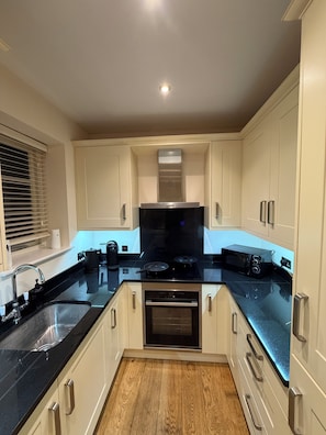 A modern kitchen with white cabinets, a black countertop, a built-in oven, and a microwave. - Contemporary Cottage - Sleeps 4 Plus Patio (Royston)