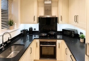A modern kitchen with a stainless steel range hood, a built-in oven, a microwave, and a sink with a faucet. - Modern Cottage Sleeps 4 With Patio (Royston)