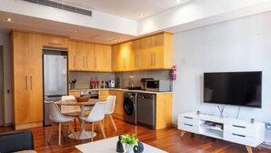 Una cocina moderna con armarios de madera, un comedor con sillas, un televisor y un mueble blanco para entretenimiento.