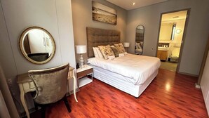 Un dormitorio con cama, una silla, una mesita de noche, un espejo y un cuadro en la pared.