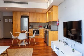 Eine moderne Küche mit Holzschränken, Edelstahlgeräten, einem Essbereich mit weißen Stühlen und einem an der Wand befestigten Flachbildfernseher.